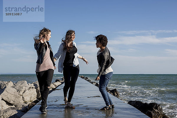 Drei junge Frauen haben Spaß auf dem Wellenbrecher am Meer