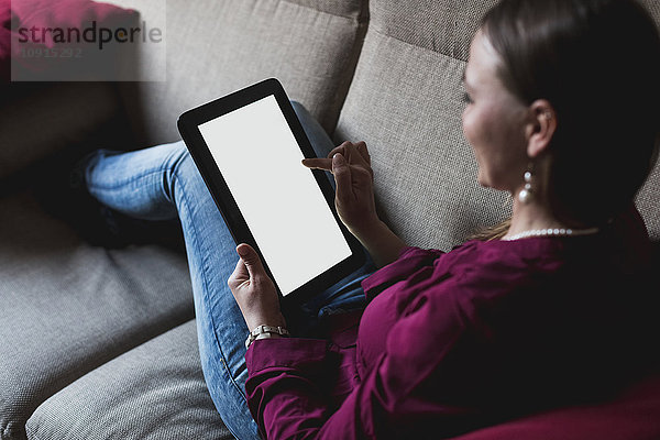 Junge Frau auf der Couch sitzend mit digitalem Tablett