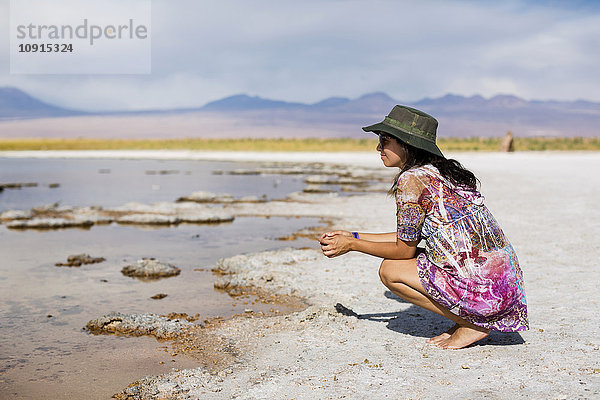 Chile  San Pedro de Atacama  Frau in der Wüste am Seeufer kauernd