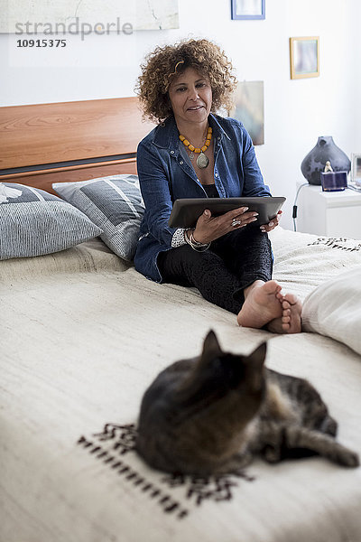 Frau mit Katze auf dem Bett mit digitalem Tablett