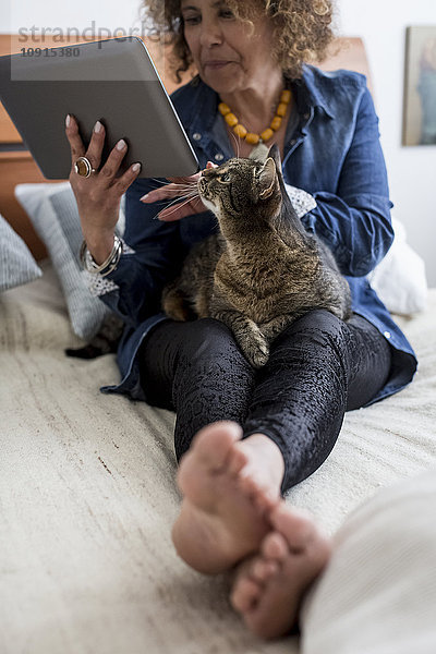 Frau mit Katze auf dem Bett mit digitalem Tablett