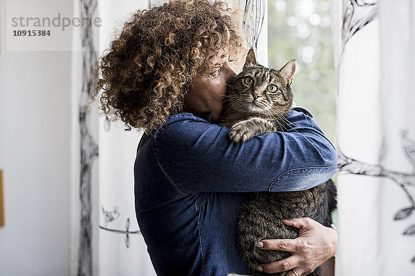 Frau kuschelt mit Katze am Fenster