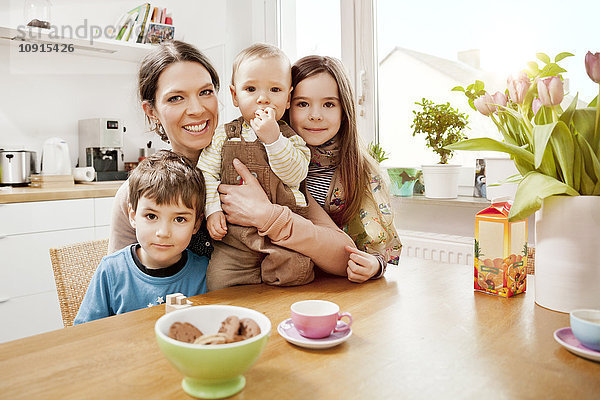 Porträt der glücklichen Mutter mit ihren drei kleinen Kindern in der Küche