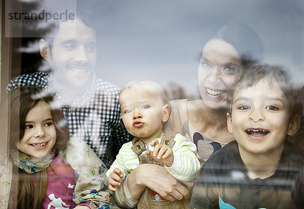 Glückliche fünfköpfige Familie mit Blick durch die Fensterscheibe