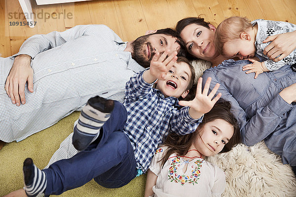 Familie mit drei Kindern  die zu Hause auf dem Boden liegen und auf die Kamera schauen.