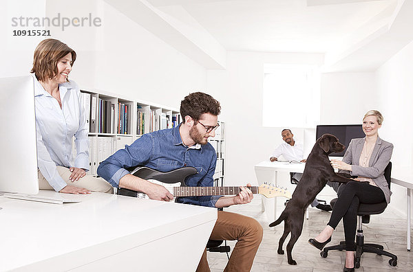 Drei Leute im Büro  die ihrem Kollegen beim Gitarrespielen zuhören.