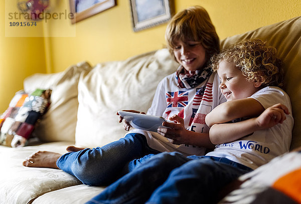 Zwei Jungen sitzen auf der Couch und benutzen ein digitales Tablett.