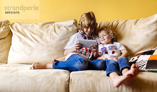 Zwei lächelnde Jungen sitzen auf der Couch und benutzen ein digitales Tablett.