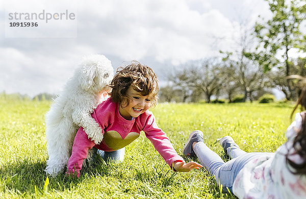 Zwei kleine Schwestern  die mit ihrem Hund auf einer Wiese spielen.