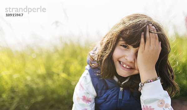 Porträt eines lächelnden kleinen Mädchens  das das Auge mit der Hand bedeckt.