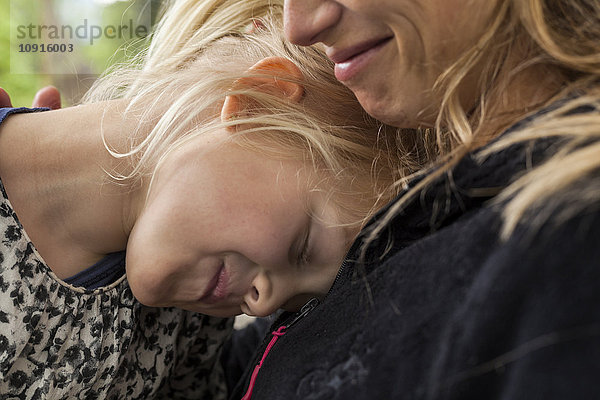 Lächelndes kleines Mädchen mit geschlossenen Augen in der Nähe ihrer Mutter