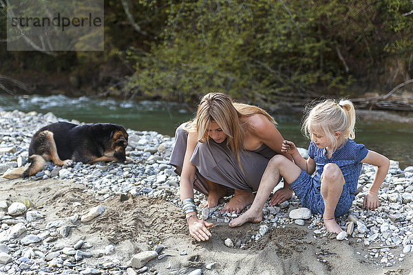 Mutter und ihre kleine Tochter spielen zusammen am Flussufer.