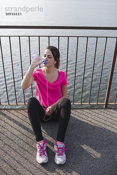 Sportliche junge Frau trinkt Wasser nach dem Laufen am Seeufer