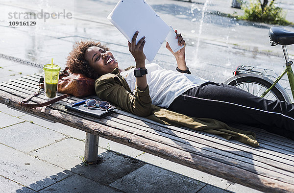 Lächelnde Frau liegt auf einer Bank und liest Notizen.