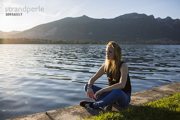 Italien  Lecco  nachdenkliches Teenagermädchen am Ufer des Sees sitzend