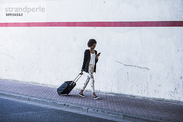 Gehende Geschäftsfrau mit Gepäck beim Blick auf ihr Smartphone