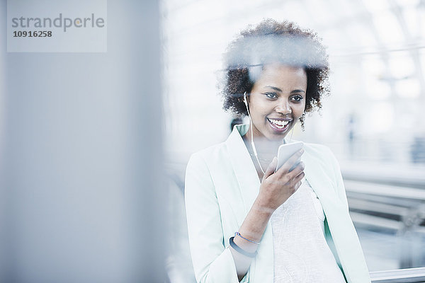 Porträt einer lächelnden jungen Frau mit Kopfhörer und Smartphone auf der Plattform