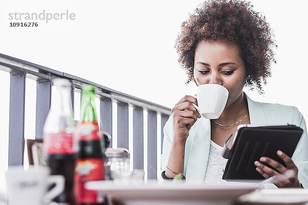 Junge Frau in einem Café  die Kaffee trinkt  während sie auf ihr digitales Tablett schaut.