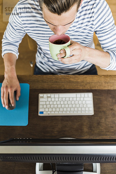 Mann mit Computer und Kaffeetrinken aus der Tasse am Schreibtisch