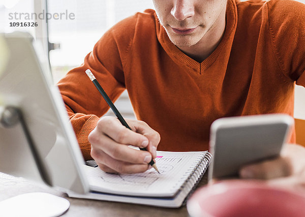 Mann am Schreibtisch mit Handy  digitalem Tablett und Notizblock