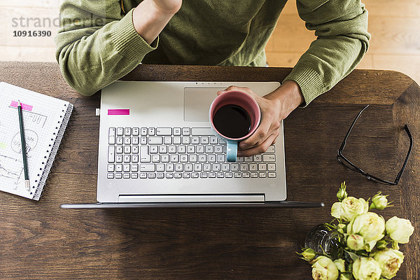 Mann am Holztisch mit Laptop und Kaffeetasse