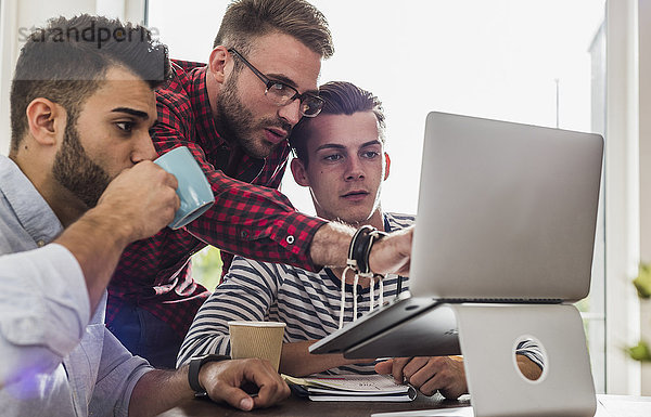 Drei junge Profis teilen sich den Laptop im Büro
