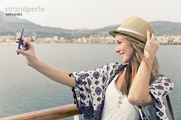 Lächelnde Frau auf dem Kreuzfahrtschiff nimmt Selfie mit Smartphone