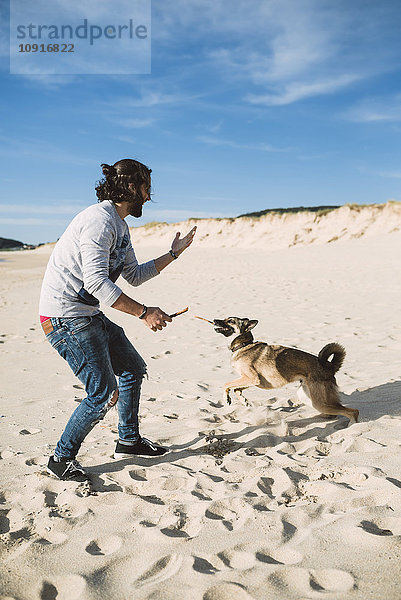 Mann  der mit seinem Mischling am Strand spielt.