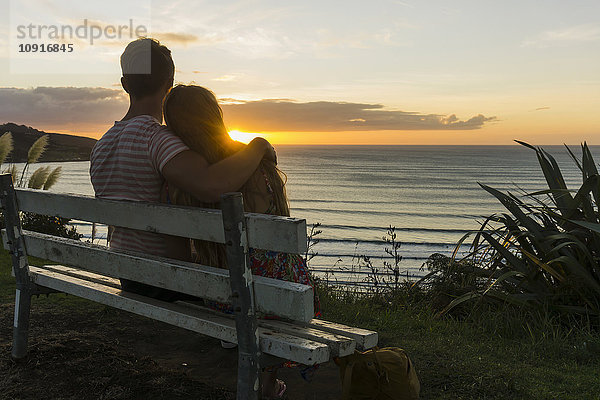 Verliebtes Paar sitzt auf der Bank und schaut auf den Sonnenuntergang.