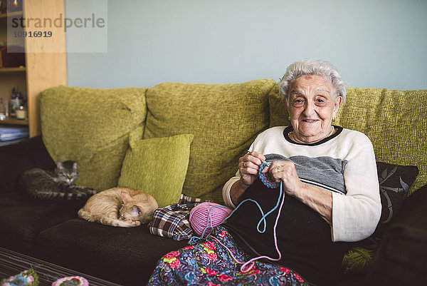 Porträt einer älteren Frau  die neben ihren schlafenden Katzen auf der Couch sitzt.