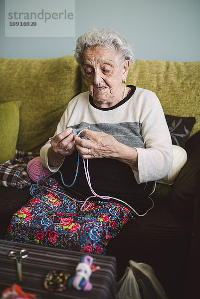 Porträt der häkelnden Seniorin  die zu Hause auf der Couch sitzt.