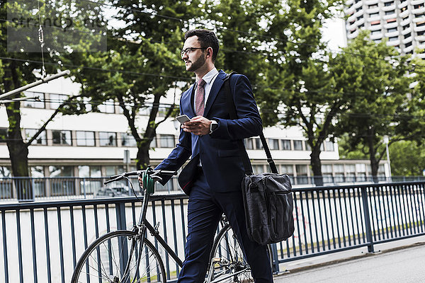 Geschäftsmann mit Fahrrad zu Fuß in der Stadt  mit Smartphone