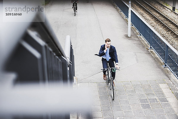 Junger Geschäftsmann auf dem Fahrrad beim Telefonieren