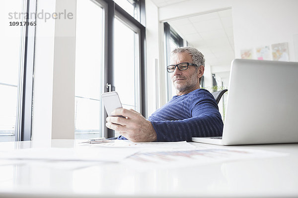 Erwachsener Mann sitzt im Büro mit Laptop  mit Smartphone