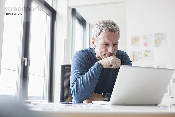 Erwachsener Mann sitzt im Büro mit Laptop