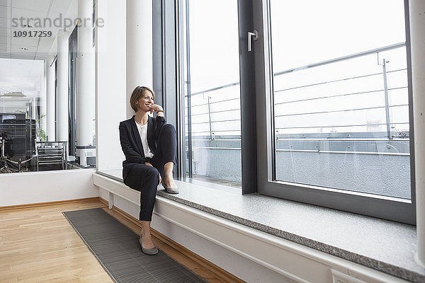 Lächelnde Geschäftsfrau auf der Fensterbank sitzend