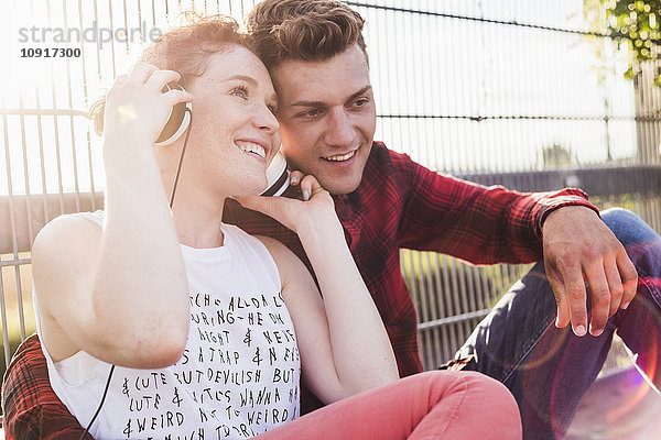 Lächelndes junges Paar am Zaun mit Kopfhörer