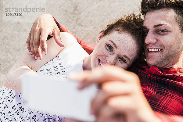 Lächelndes junges Paar im Liegen mit einem Selfie