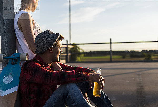 Junges Paar mit Skateboard und Bierflasche beim Sonnenuntergang