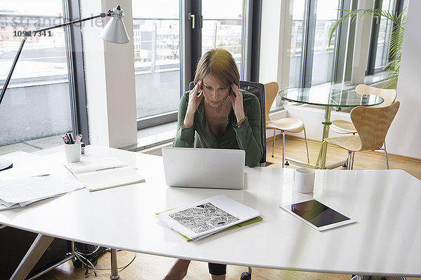 Konzentrierte Geschäftsfrau bei der Arbeit am Laptop am Schreibtisch