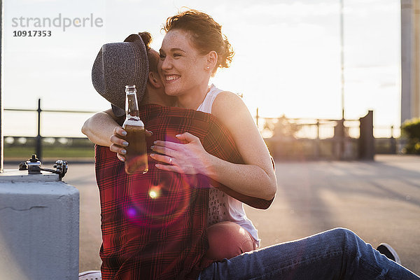 Glückliches junges Paar mit Bierflaschenumarmung bei Sonnenuntergang