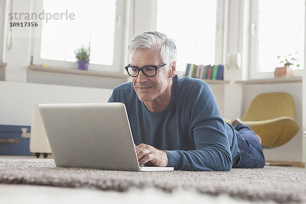 Erwachsener Mann zu Hause auf dem Boden liegend mit Laptop
