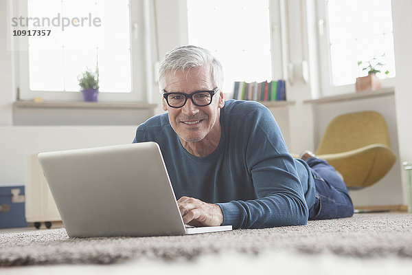 Erwachsener Mann zu Hause auf dem Boden liegend mit Laptop