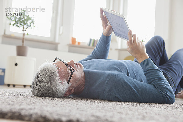 Erwachsener Mann zu Hause auf dem Boden liegend mit digitalem Tablett