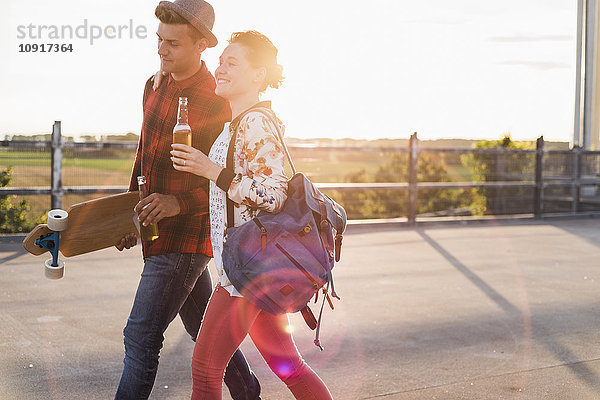 Junges Paar mit Bierflaschen und Skateboard bei Sonnenuntergang