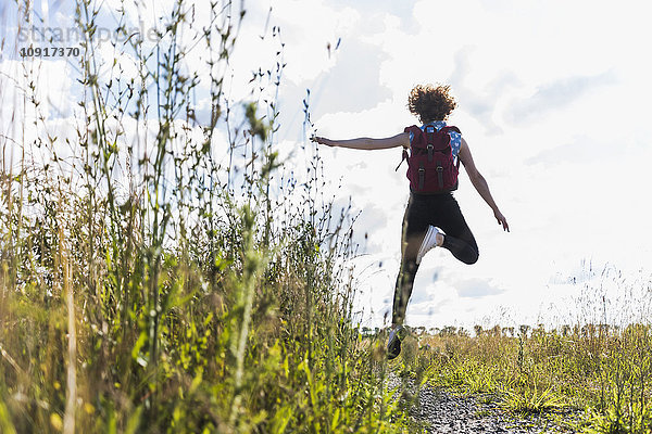 Begeisterte junge Frau beim Springen auf dem Feldweg