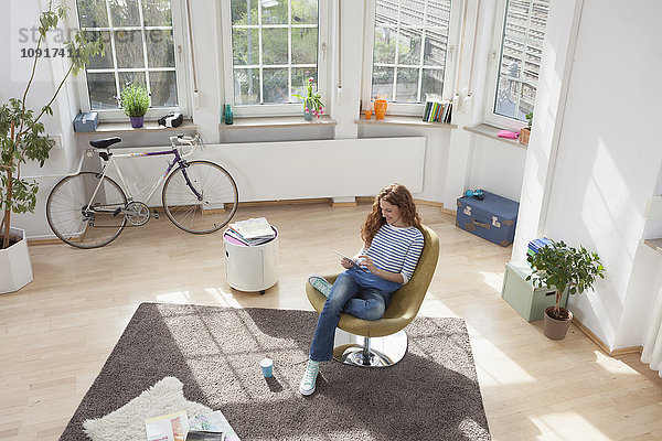 Frau zu Hause im Sessel sitzend mit digitalem Tablett