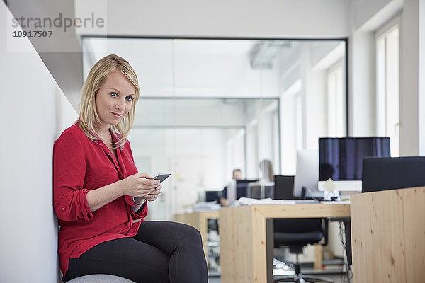 Frau im Büro sitzend mit Smartphone