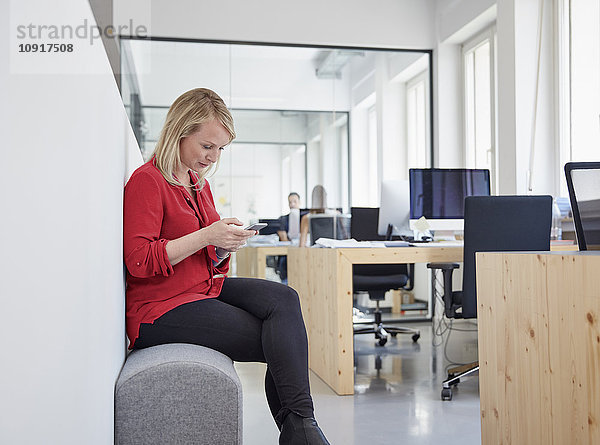 Frau im Büro sitzend mit Smartphone