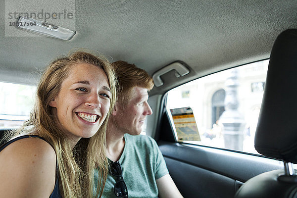 Porträt einer grinsenden Frau im Taxi mit ihrem Freund im Hintergrund